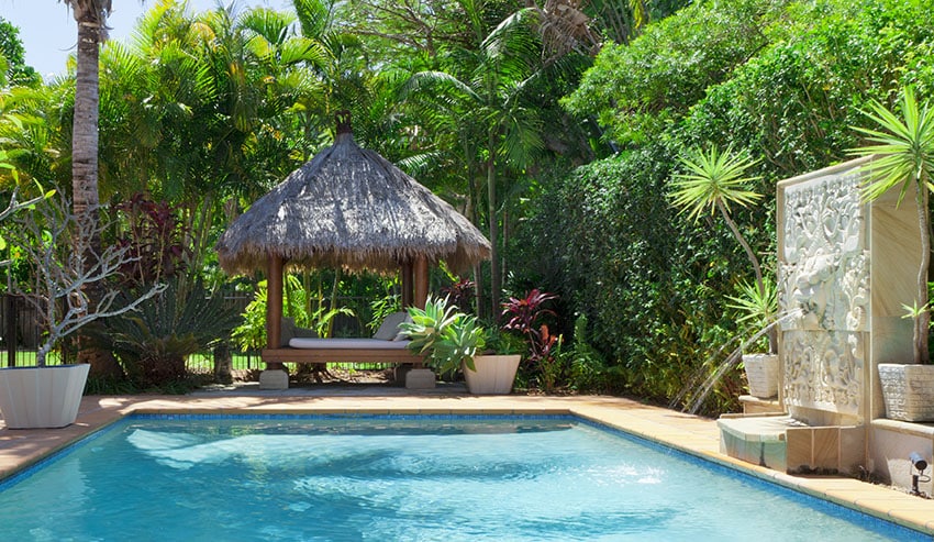 Backyard with swimming pool and thatched cabana with daybed