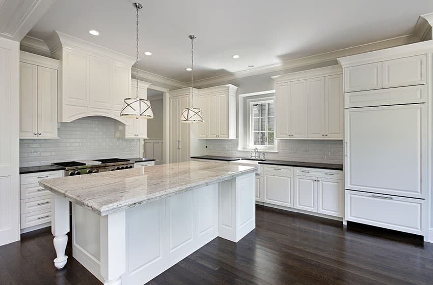 White kitchen with white subway tiles, large island, granite counters and drum pendant lights