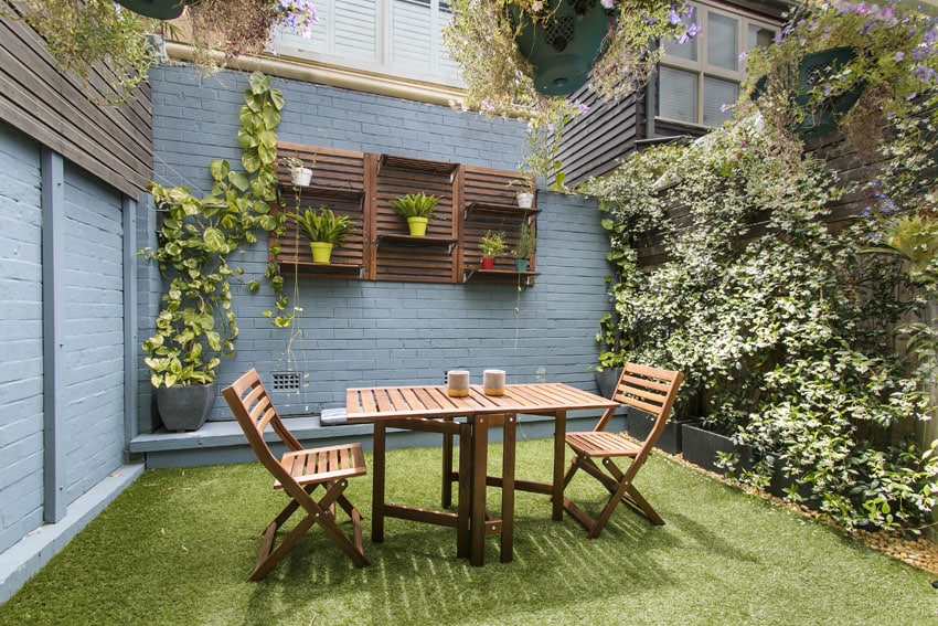 Backyard patio with brick wall and wood shelving with potted plants