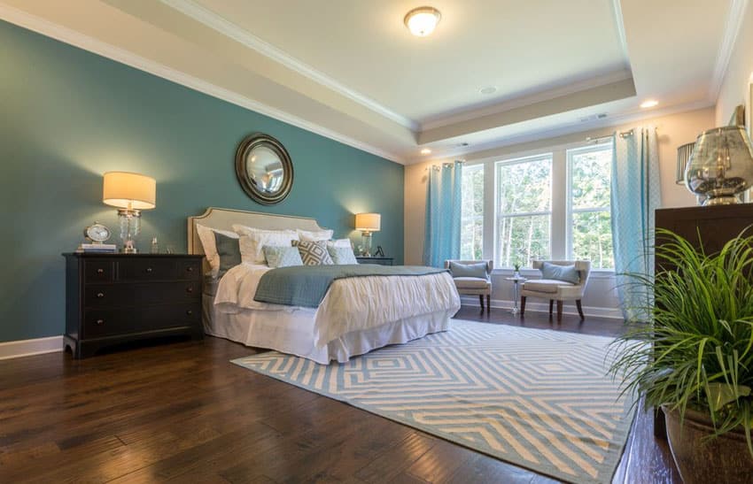 Beautiful bedroom with blue green painted accent wall, white room paint, window sitting area and wood flooring