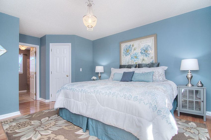 Beautiful blue and white bedroom with light wood flooring and light brown flower area rug