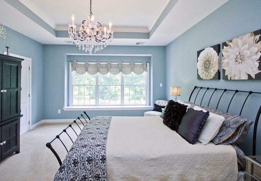 Beautiful blue bedroom with white tray ceiling, hanging chandelier and artwork