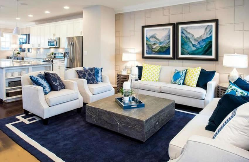 Open plan layout with dark blue rug, white sofa set, blue pillows and recessed lights