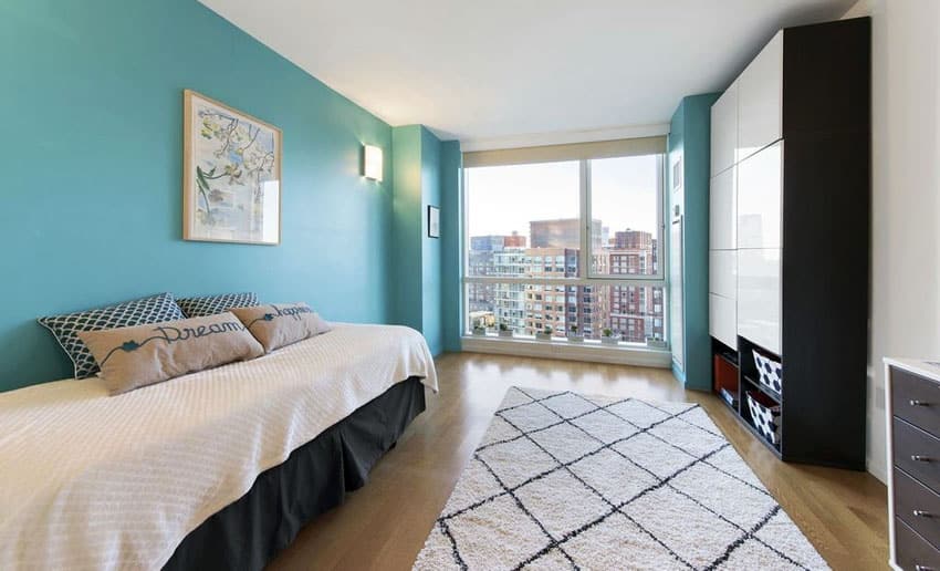 Bright blue apartment guest bedroom with twin bed and light wood floors