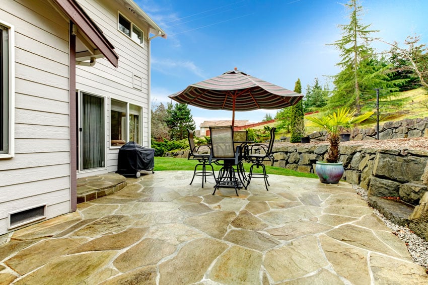 Cozy backyard flagstone patio with stone retaining wall and outdoor dining table with umbrella