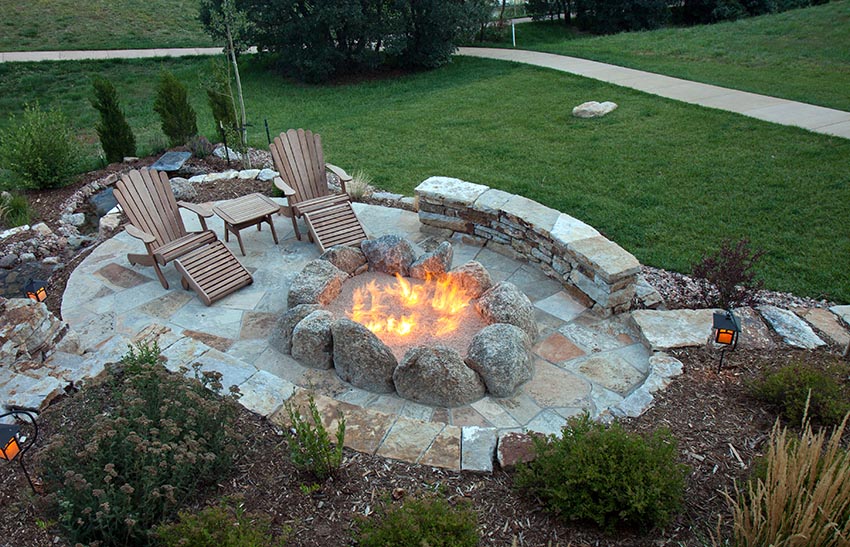 Custom rock fire pit on flagstone patio with lounge chairs surrounded by lawn
