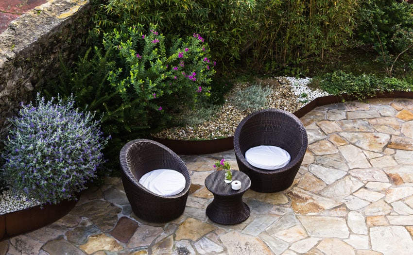 Flagstone patio with outdoor chairs and large bushes