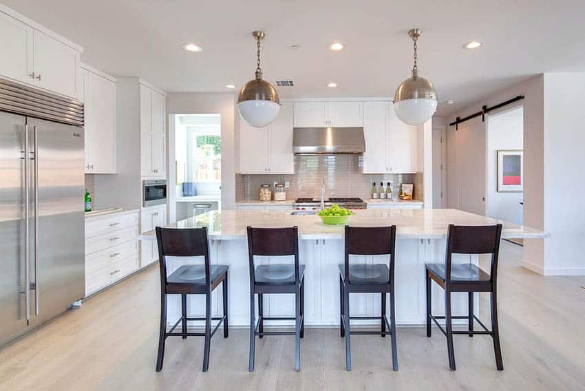 Kitchen with white cabinets, light color laminate floors and long breakfast bar island with marble countertops