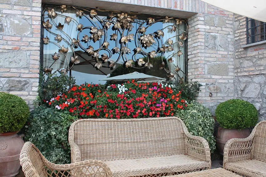 Large picture window with decorative metal design and window box flowers above patio sitting area