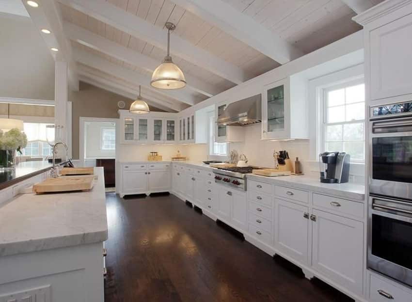 Large white contemporary kitchen with marble countertops, wood floors and white tile backsplash
