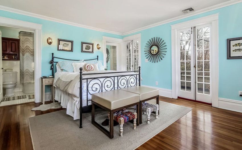 Light blue and white bedroom with wrought iron bed and hardwood flooring