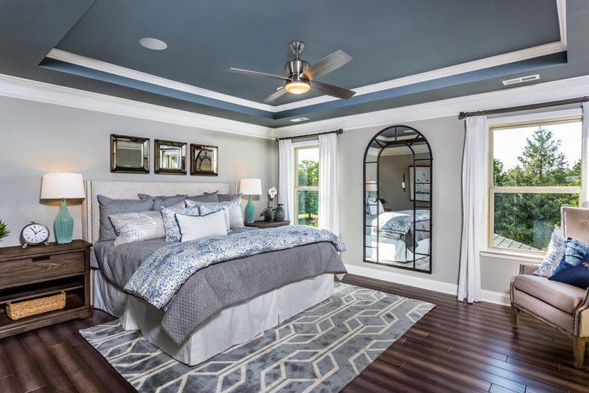 Master bedroom with light gray walls, painted blue tray ceiling and white molding with dark wood floors