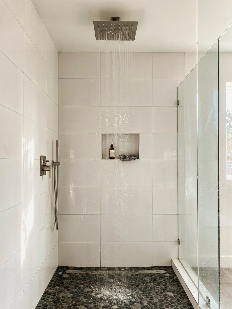 Walk in shower with white porcelain walls and dark lava stone pebble mosaic floor