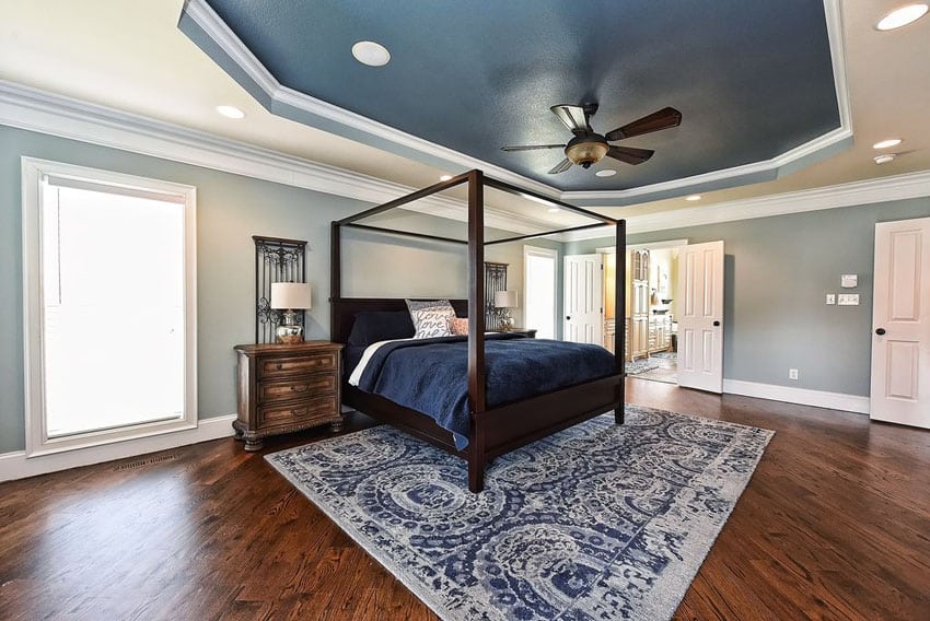 Two color blue bedroom with white trim painted tray ceiling and wood flooring