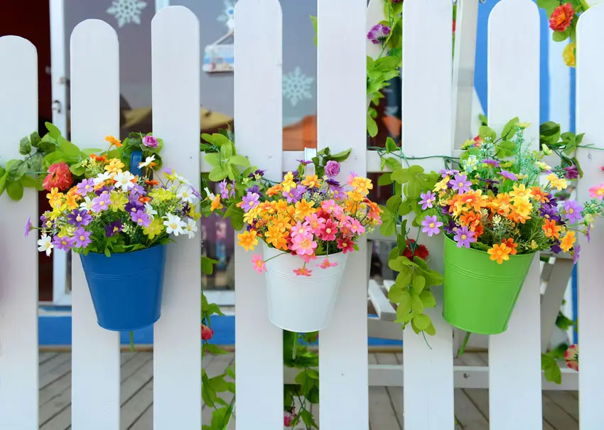 White fence with colorful hanging pots with beautiful flowers