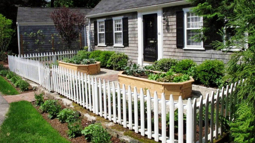White picket fence around raised garden beds in front of house