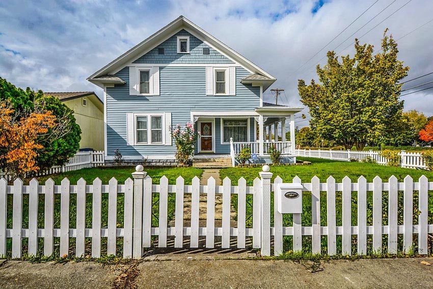 White picket fence design surrounding a charming home with large front porch