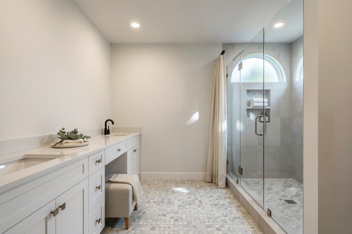 Bathroom with white and gray palette with white paneled cabinets and square ottoman