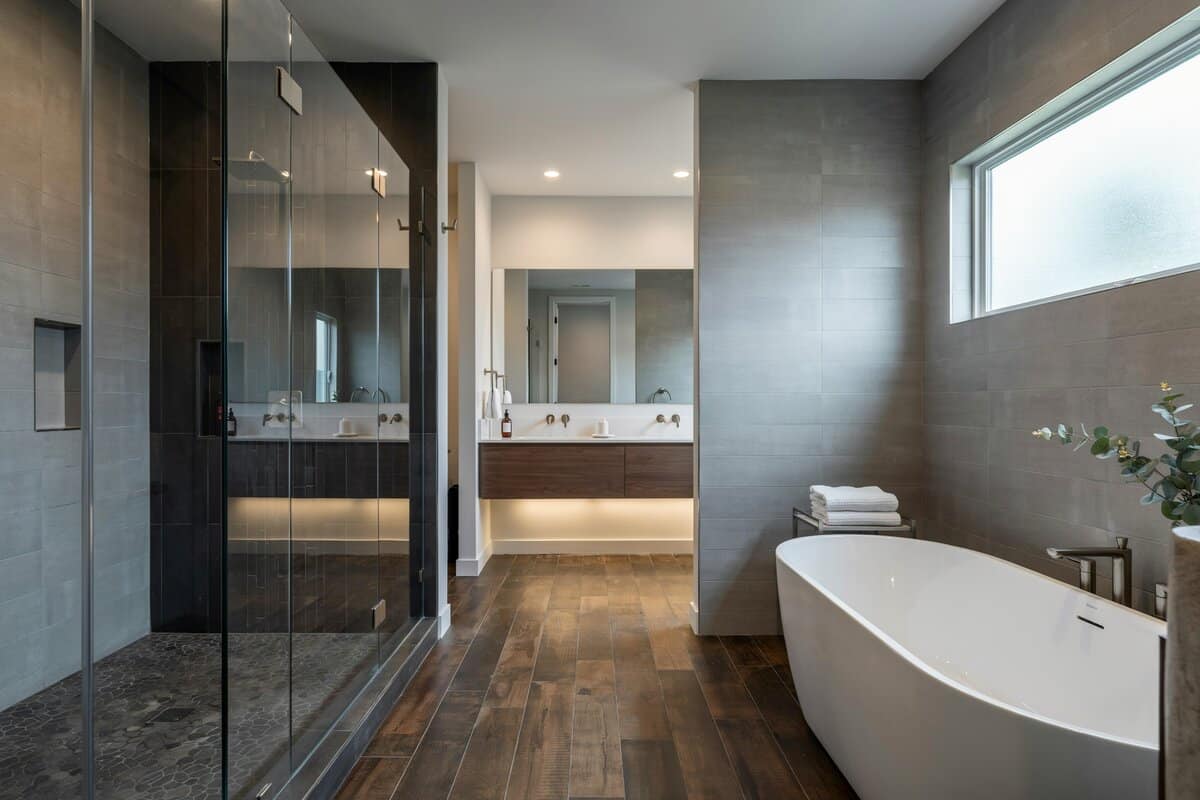 Gray bathroom with wide mirrors, enclosed bathtub and black tile shower