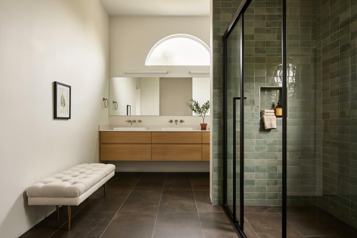 Bathroom with white tufted bench, dark colored tiles with wood vanity area