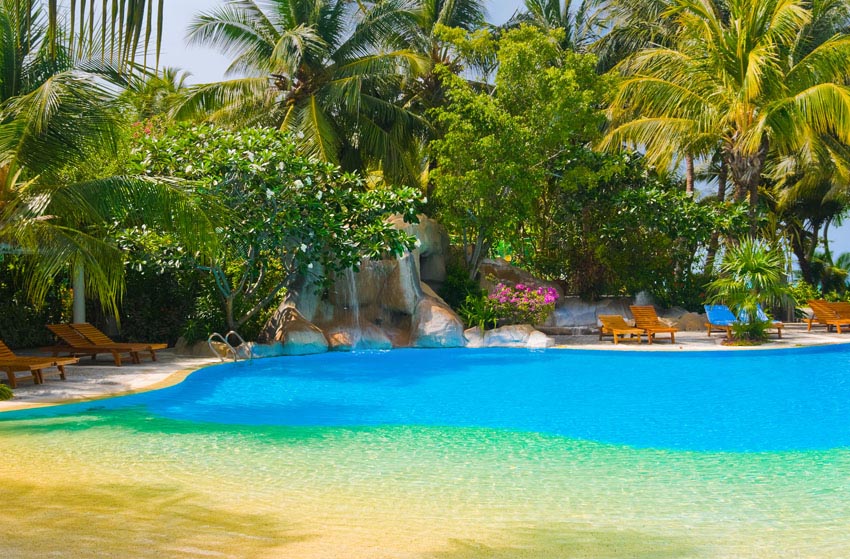 Piscina estilo laguna de entrada a la playa con paisajismo tropical