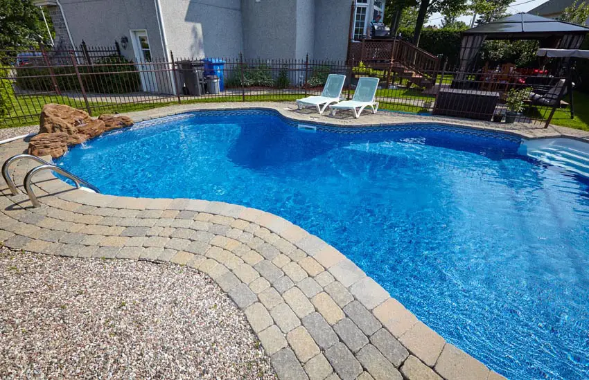 Blue kidney shaped pool with paver border