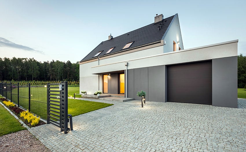 Dark brown door on modern gray home with cobblestone driveway