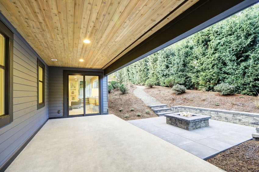 Covered patio in backyard with lower concrete level and stone firepit