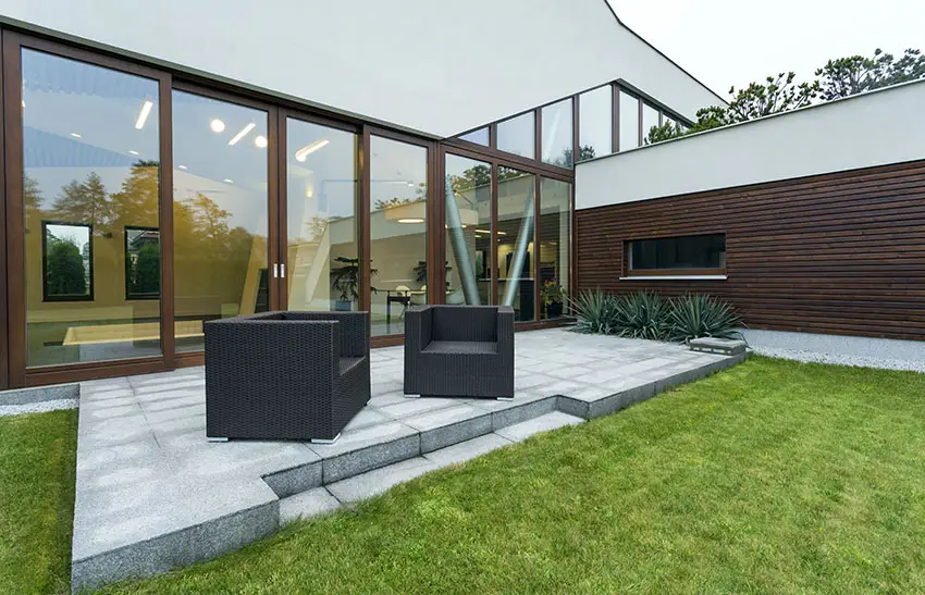 Concrete patio with window wall, rattan furniture and grass area