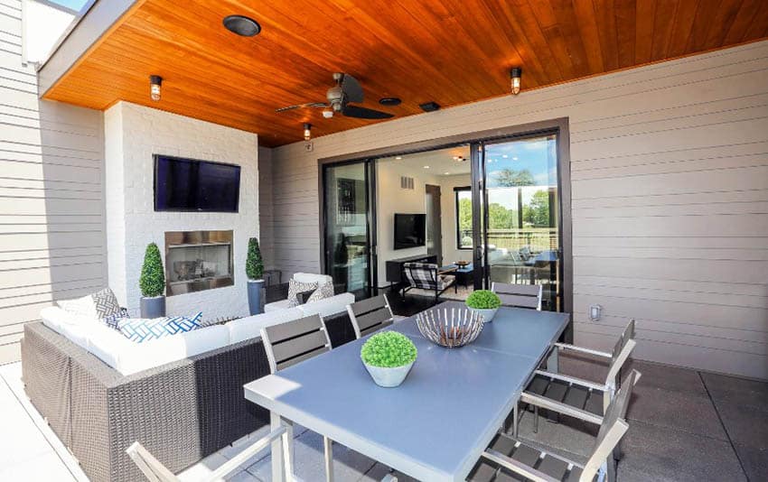 Modern covered patio with concrete flooring, outdoor dining and fireplace with flat screen tv