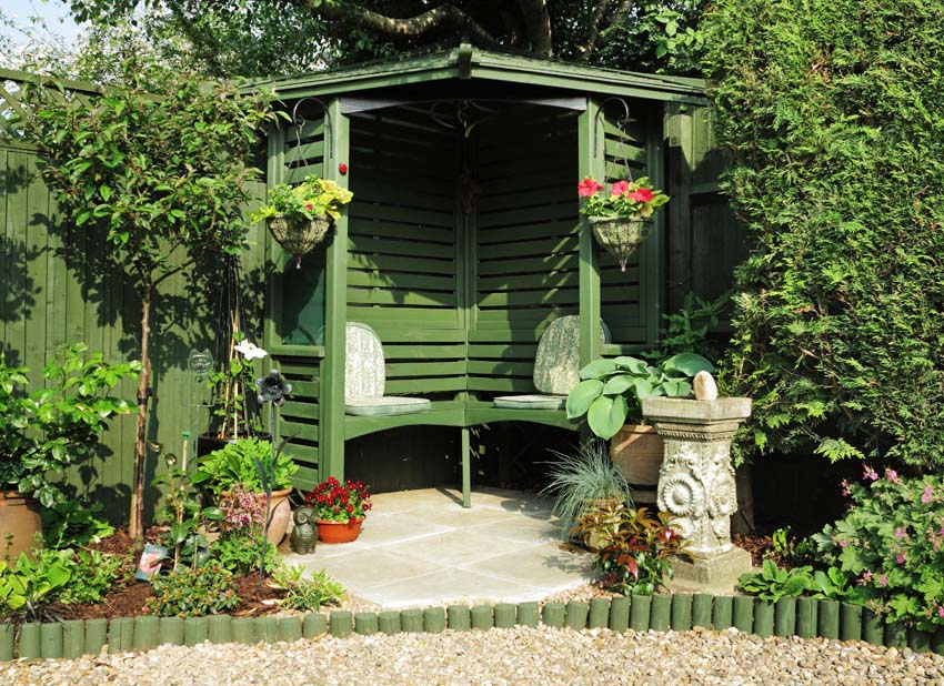 Small green garden pavilion with wood bench