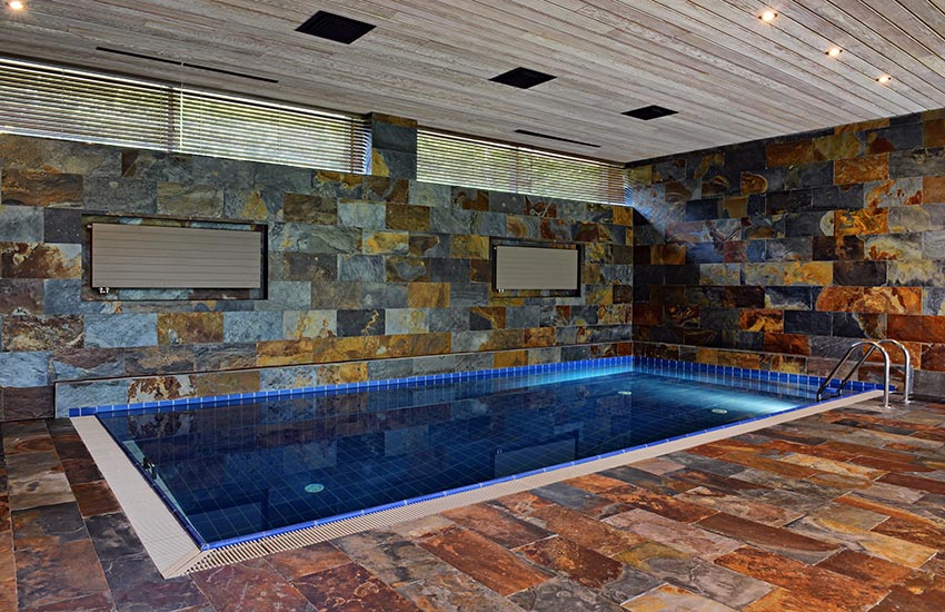 Small indoor swimming pool with blue tile and slate floors and walls