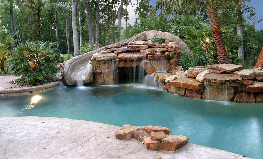 Tropical themed pool with slide and water feature and stacked boulder waterfall