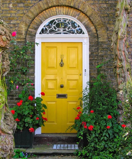 Yellow front door at rustic stone house with flowers