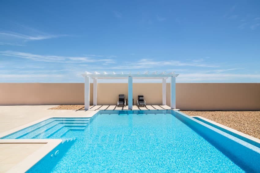 Beautiful modern blue pool with white pergola concrete patio and gravel border