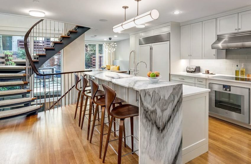 Waterfall island countertop in marble, winding staircase and steel kitchen appliances
