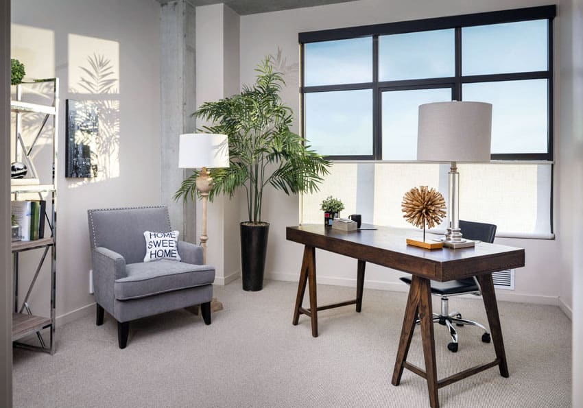 Home office with wooden desk, grey arm chair, floor lamp and steel shelves