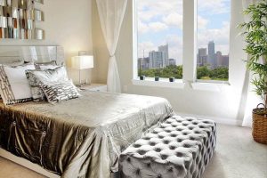 Glam bedroom with gold satin bedding and tufted ottoman