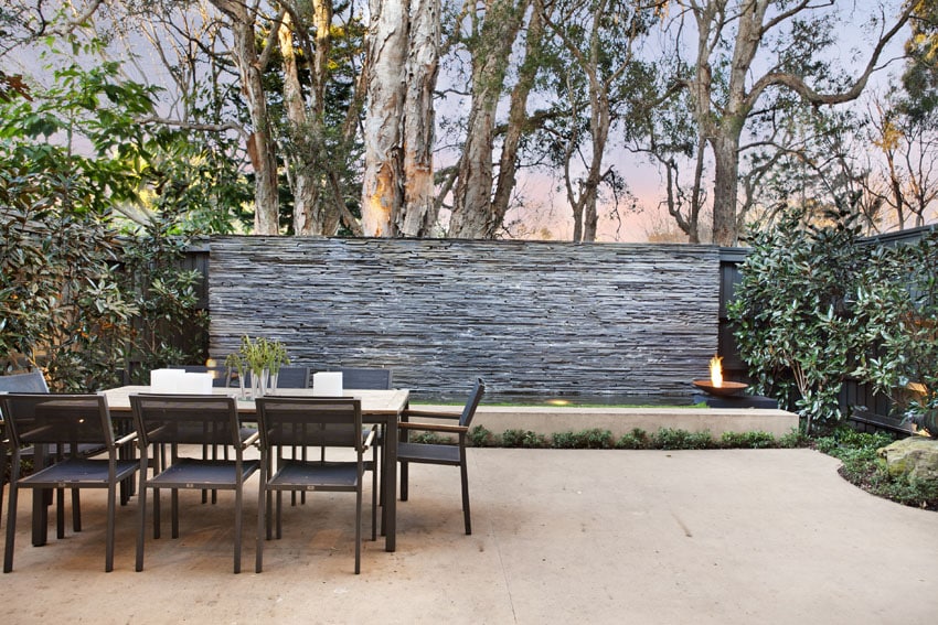 Grey slate walls, tall trees, travertine tiles and outdoor dining set