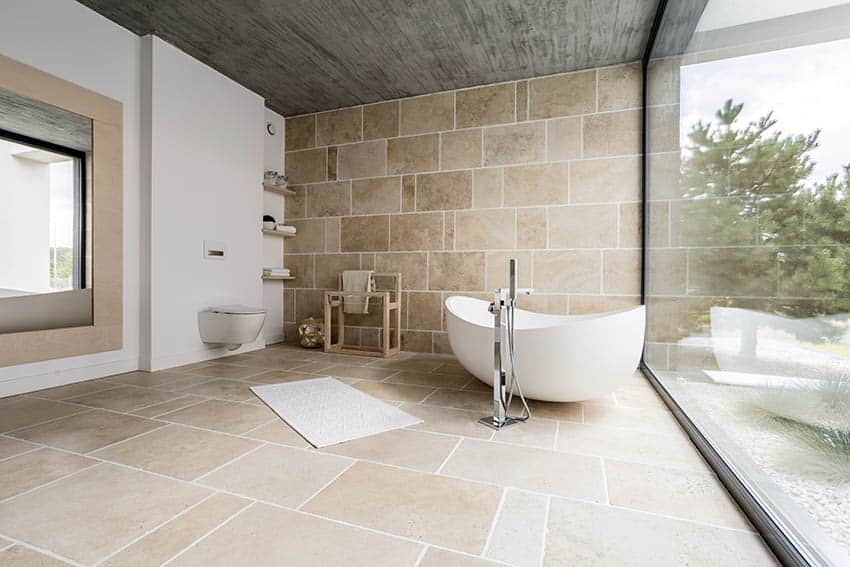 Bathroom with travertine floor tile, freestanding tub with outside views