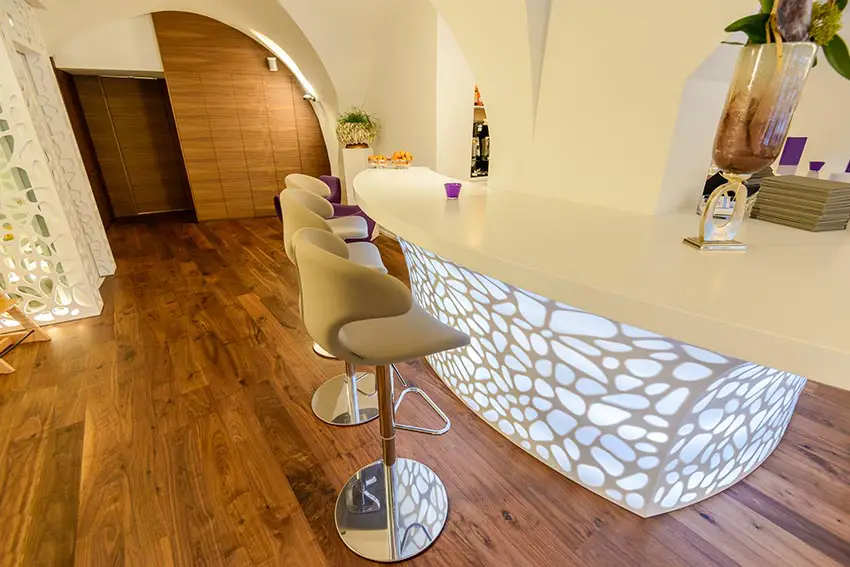 Corian topped bar with lighted base, upholstered velvet chairs and wooden floor