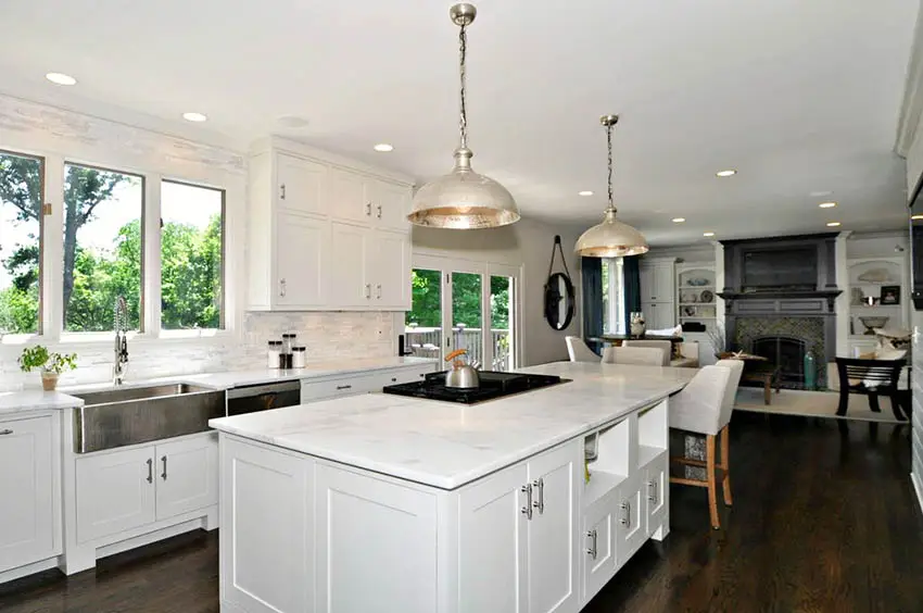 Kitchen with wooden flooring, white shaker cabinets, carrara marble backsplash, and countertops
