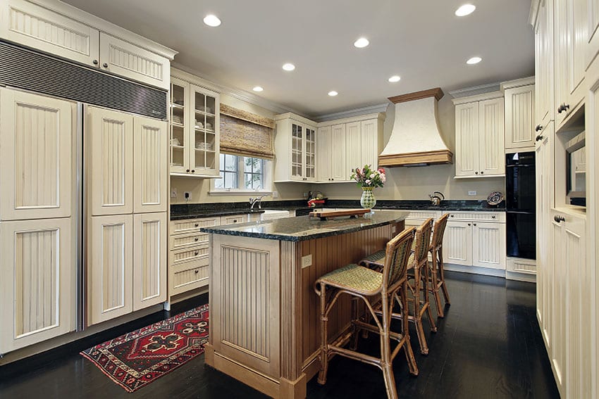 Country style kitchen with beadboard panel cabinets and beadboard island with dark wood floor