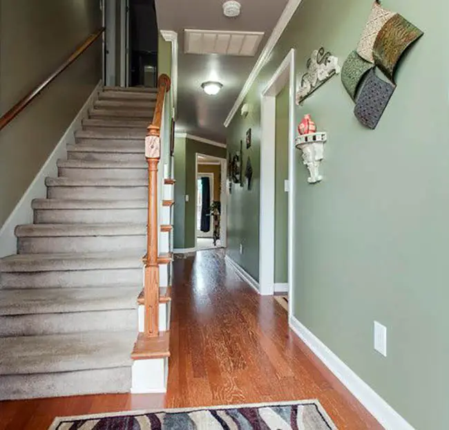 Hallway with walls in muted green, white painted moldings and staircase with wooden railings