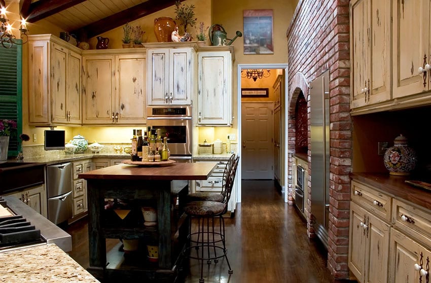 Cocina con gabinetes de madera envejecida, pared de acento de ladrillo y isla de bloques de carnicero