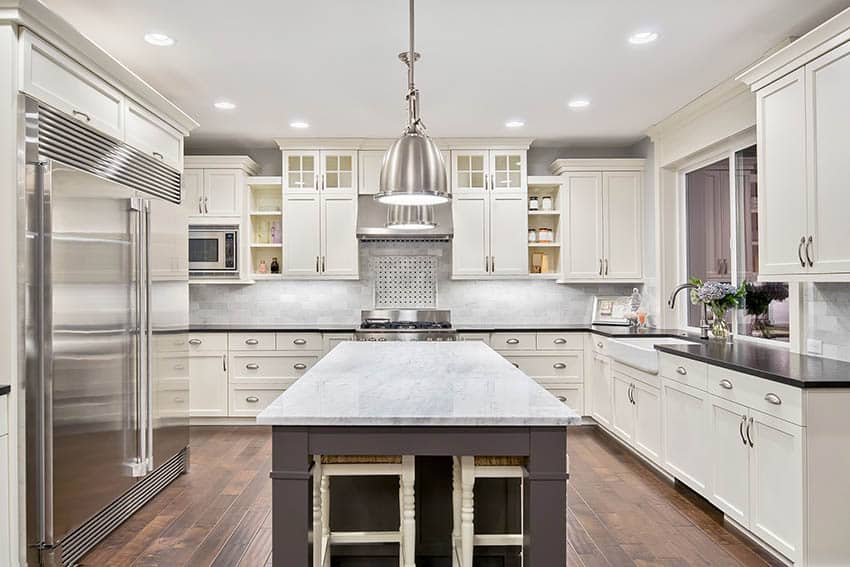 Kitchen with white shaker cabinets dark island and marble countertops