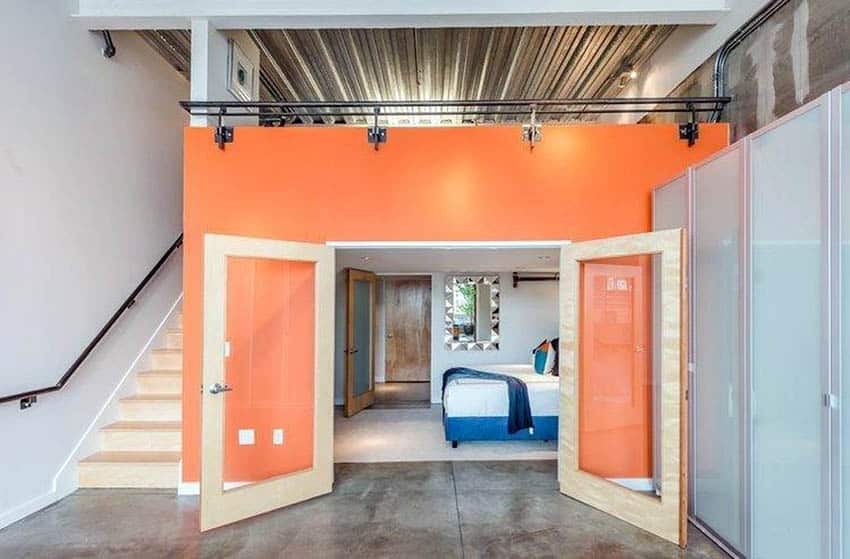 Loft bedroom with orange painted wall and gray concrete floors 