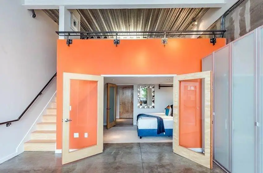 Loft bedroom with orange painted wall, concrete floors and corrugated metal ceiling