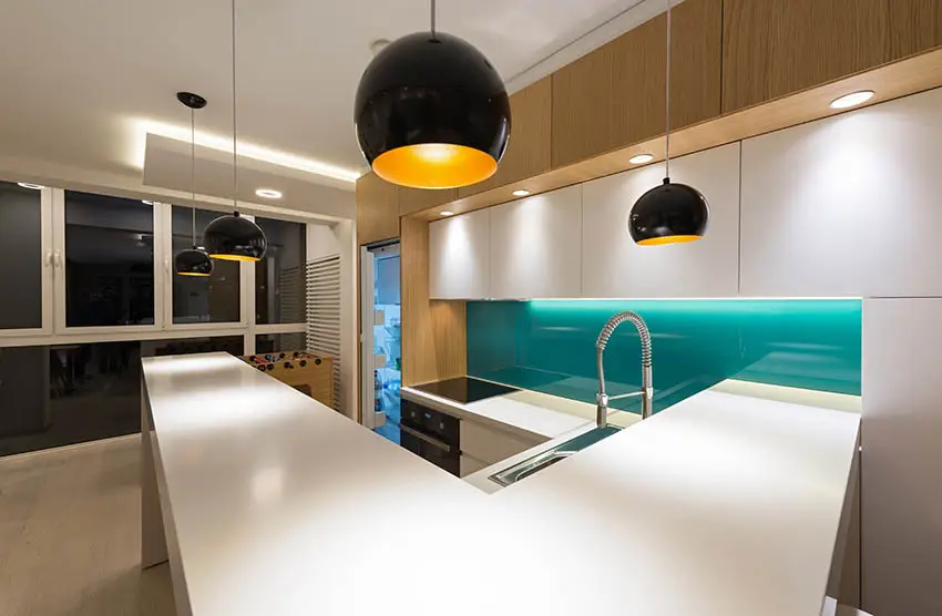 Kitchen with green glass backsplash and drum pendant lights and L-shaped counter