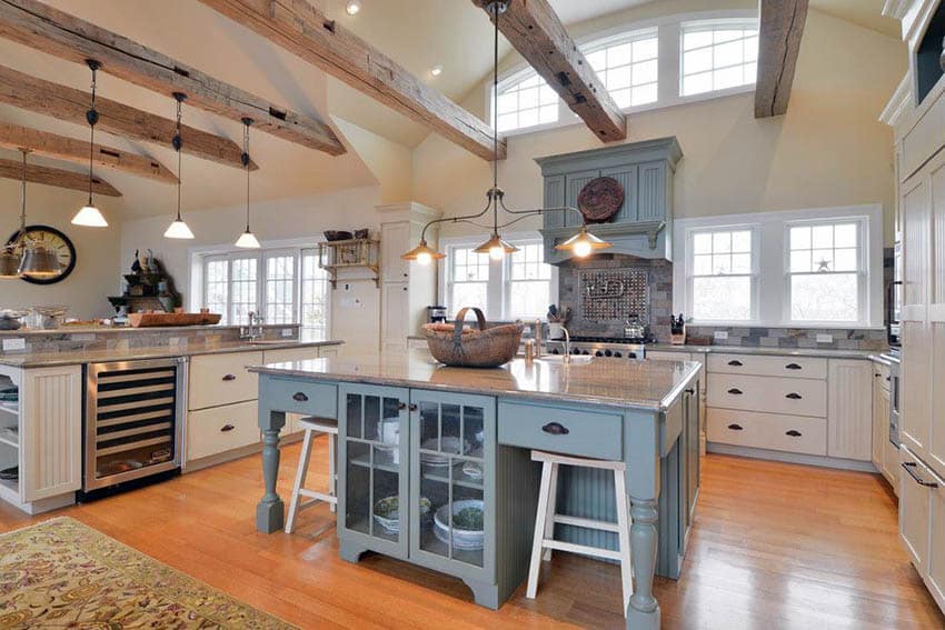 Country kitchen with white cabinets, exposed beams, wood flooring and pastel painted island